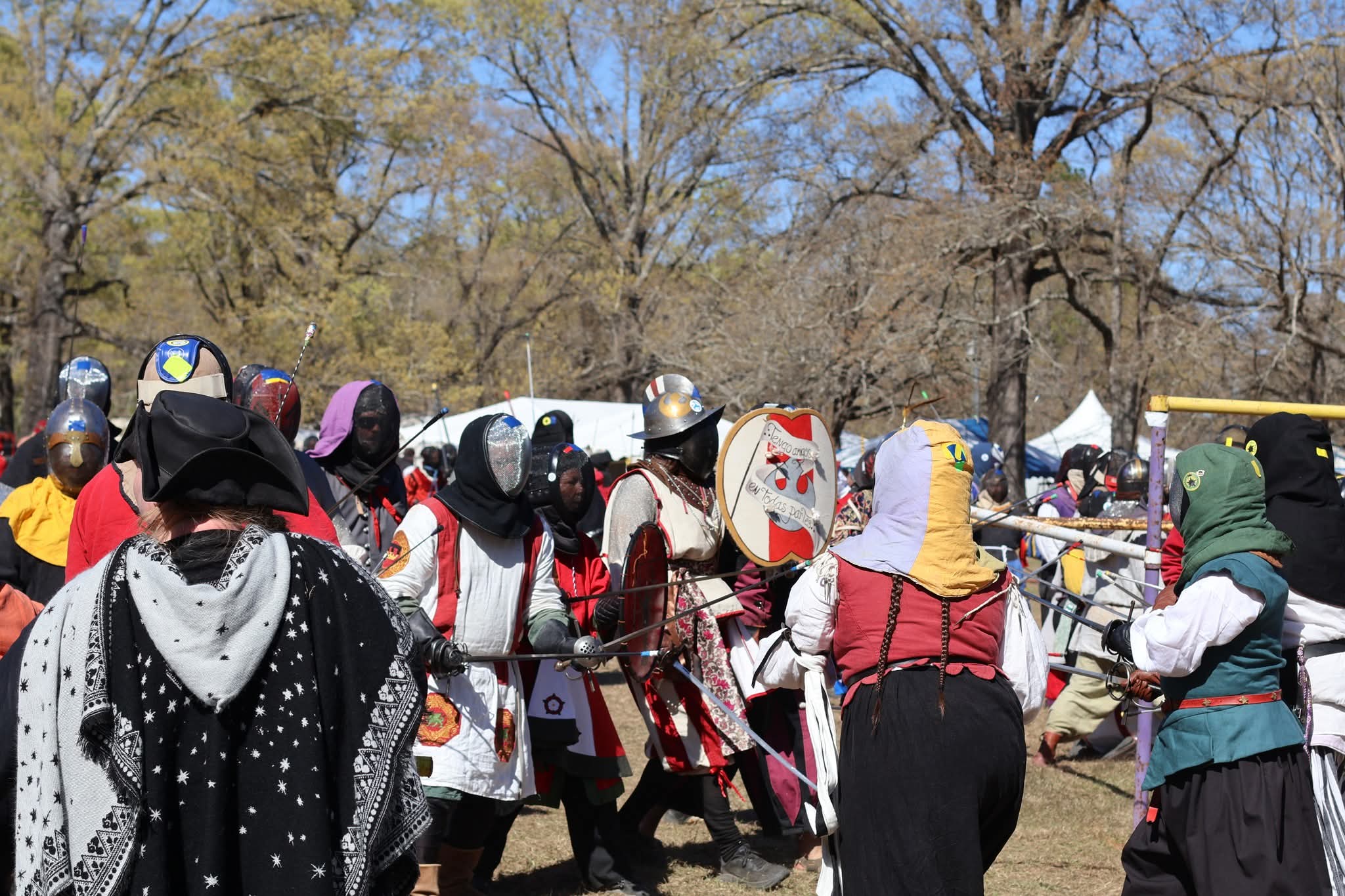 Photo of members of the Society for Creative Anachronism engaging in a combat simulation. They are wearing colorful historical costumes and protective gear.